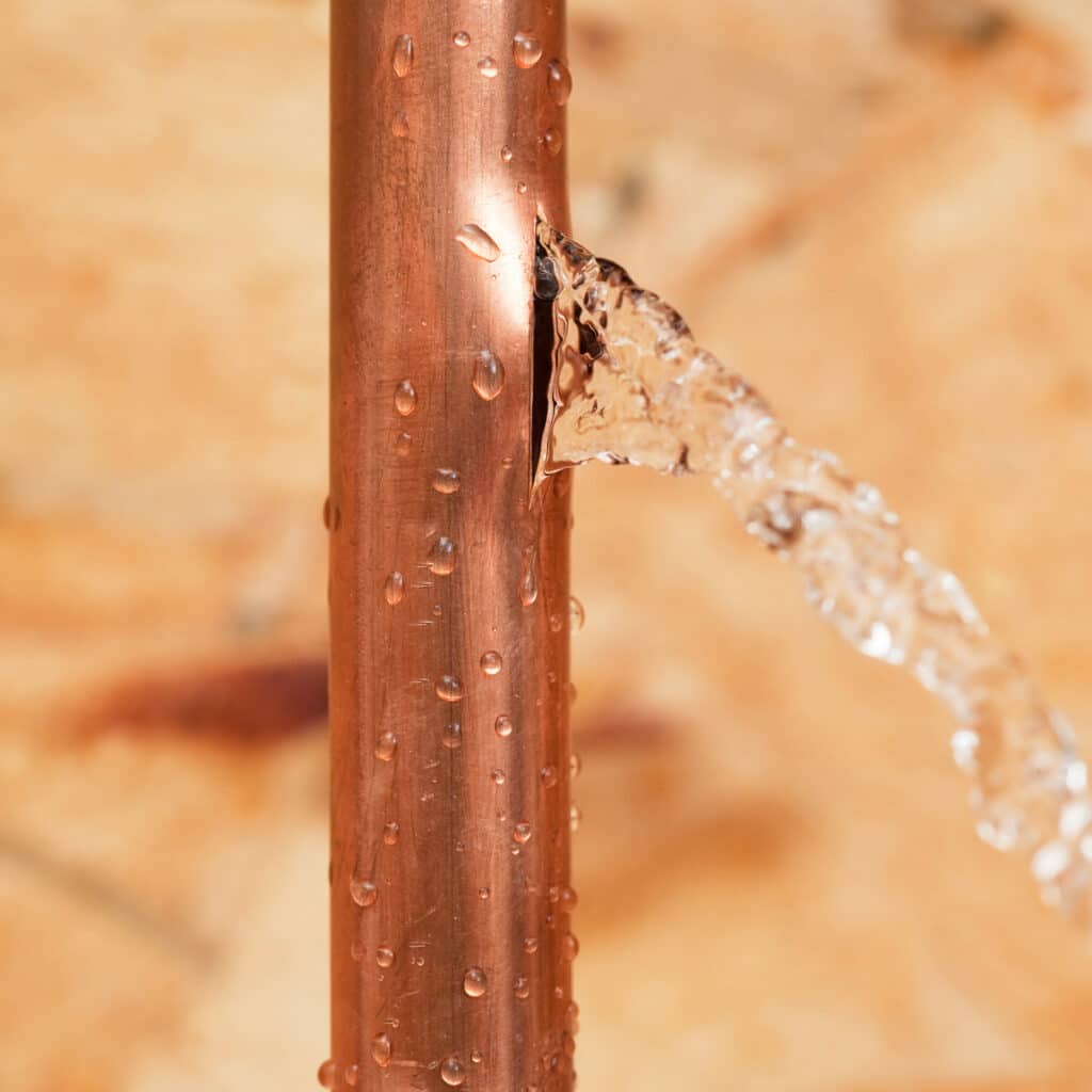 Water spraying from a burst copper pipe causing an active plumbing leak in a home.