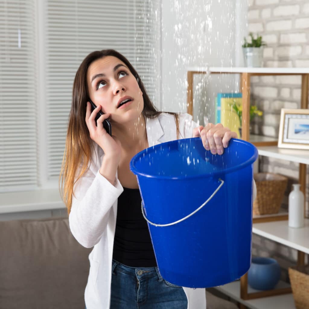 Homeowner catching water leak with bucket during plumbing emergency in house