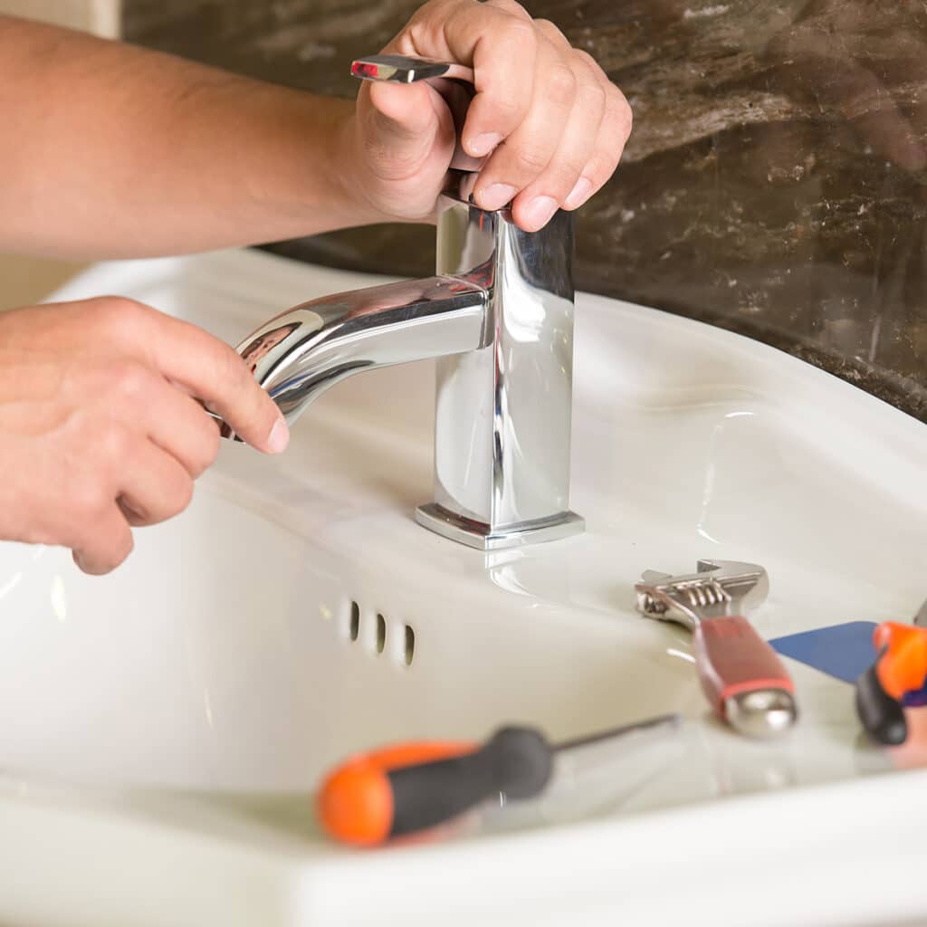 Plumber repairing bathroom faucet with tools to fix leak or handle issue