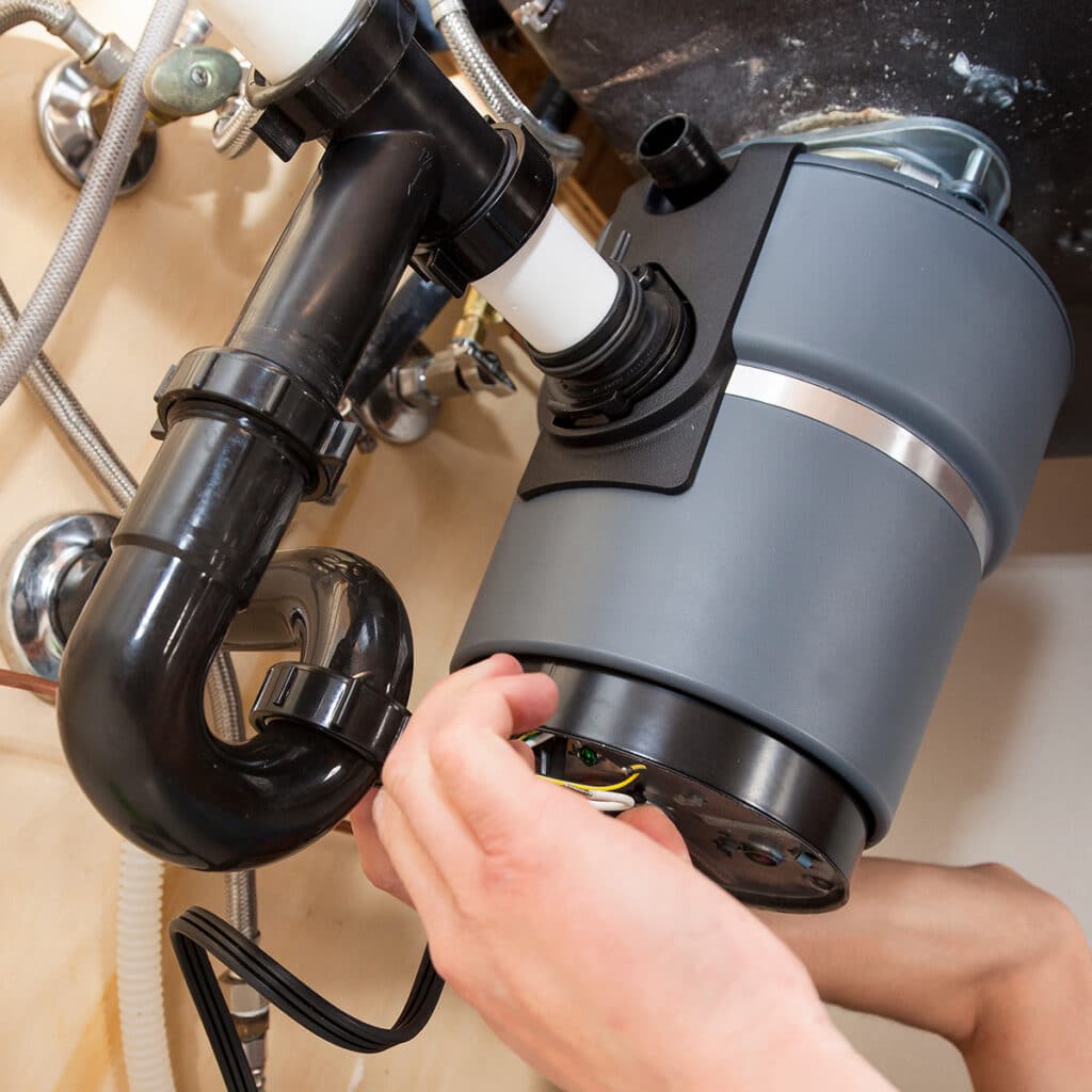 Plumber installing garbage disposal under kitchen sink with plumbing connections