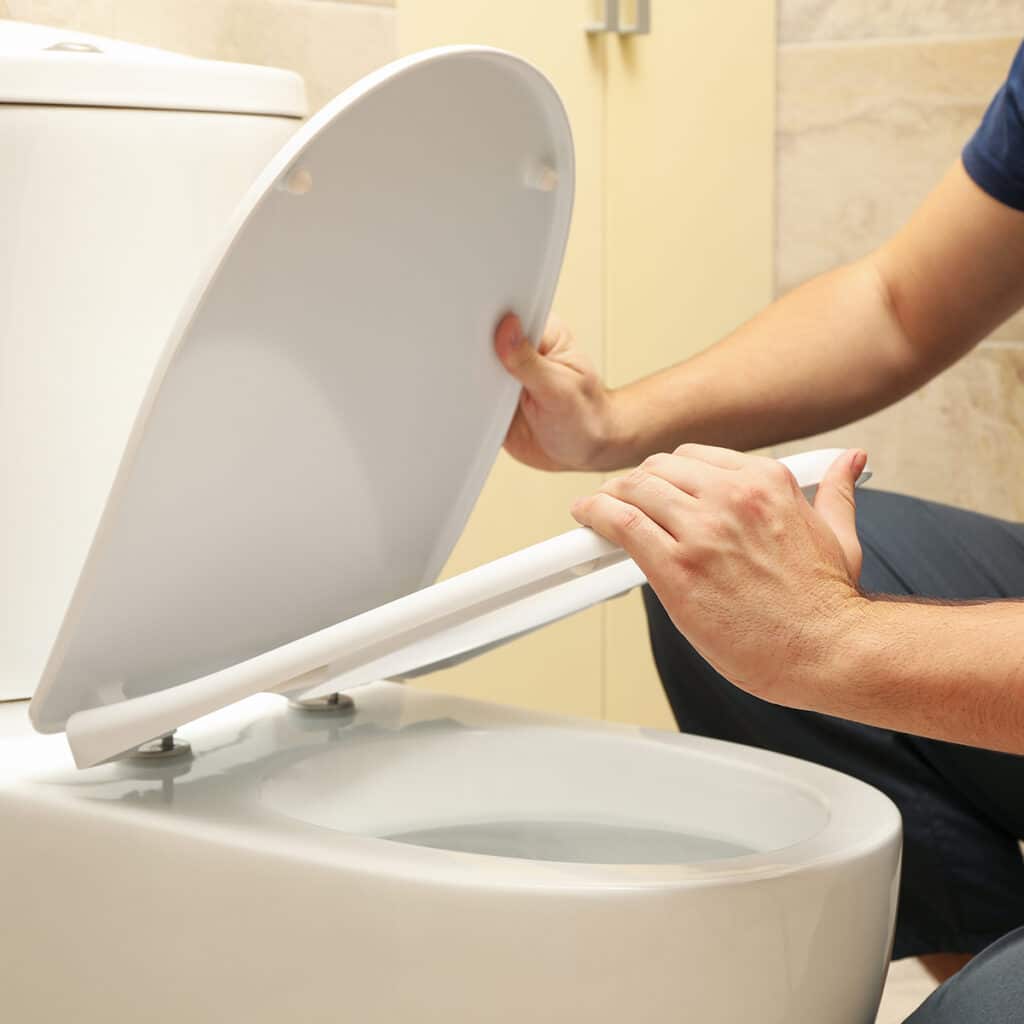 Plumber repairing toilet seat and inspecting toilet components for proper function